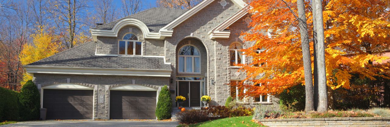 two story brick home, tree of orange leaves, yellow flowers on porch