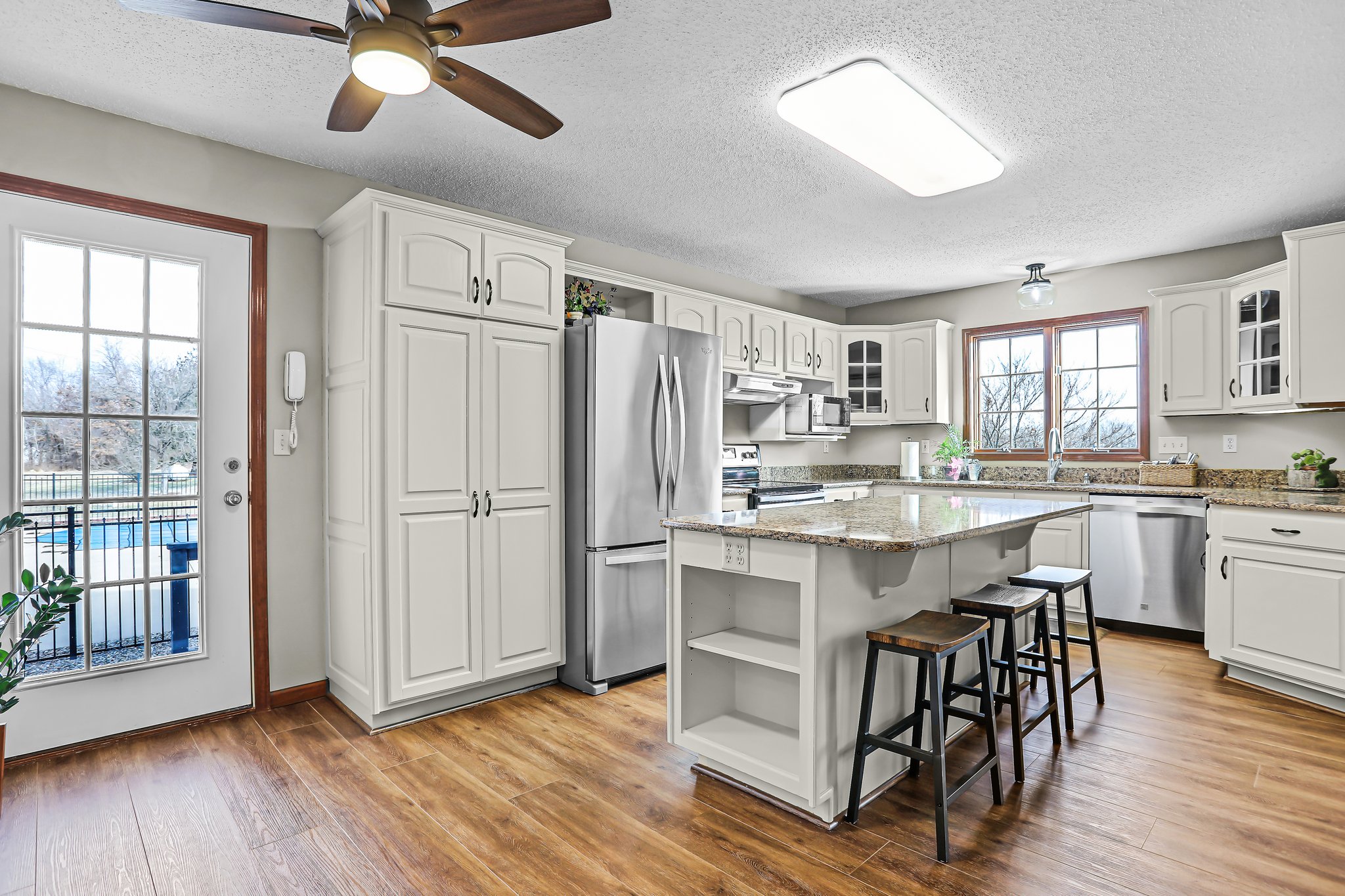 Home kitchen, with off-white cabinetry, stainless steel appliances, center island, glass front cabinets, Cambria quartz countertops, and luxury vinyl plank/wood-style flooring