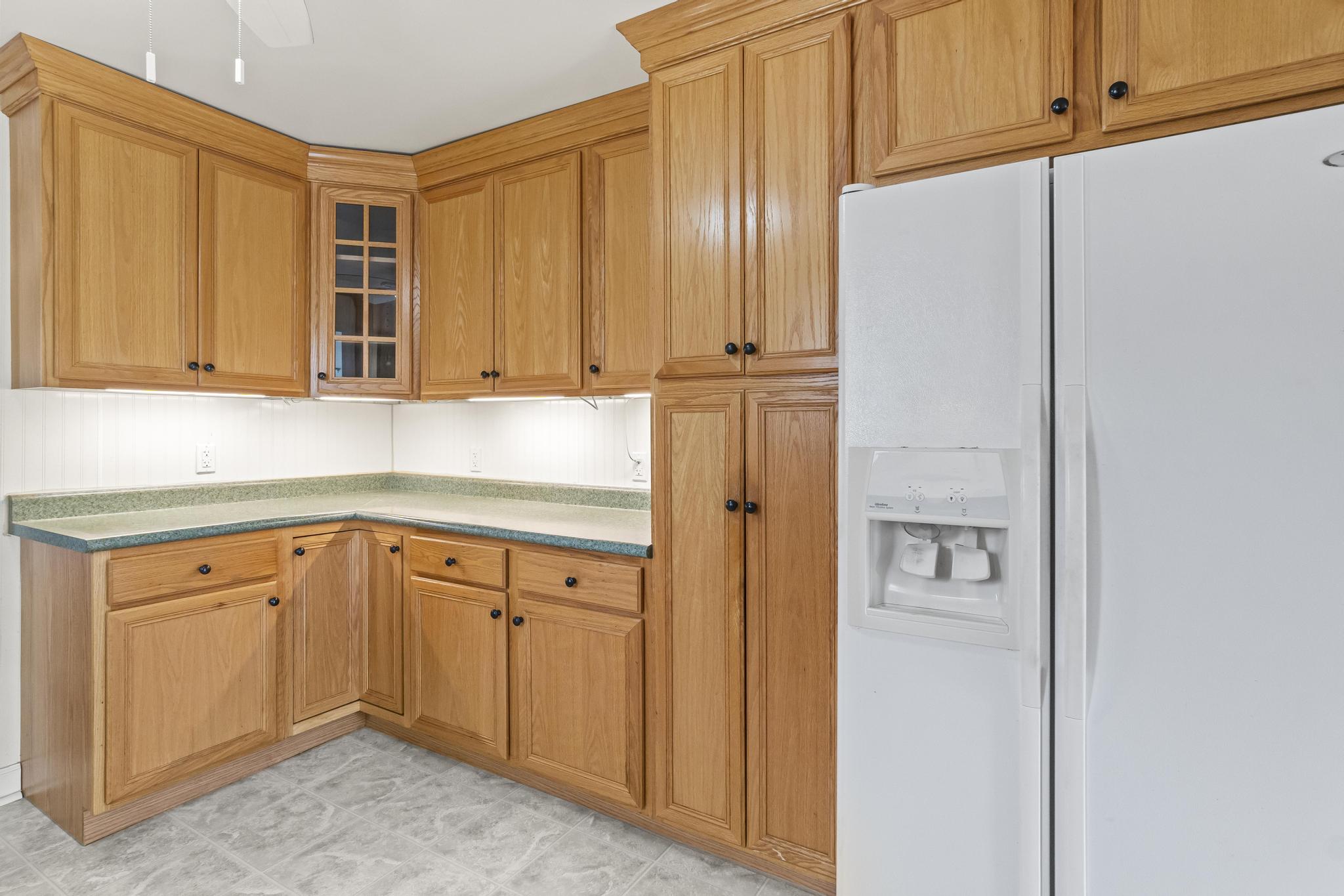 Kitchen with refrigerator, updated light cabinetry with under cabinet lighting, glass cabinet front and light colored flooring