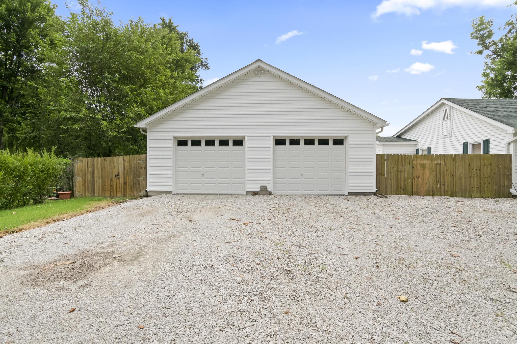 Front view of detached two bay garage and privacy fencing, with gravel driveway