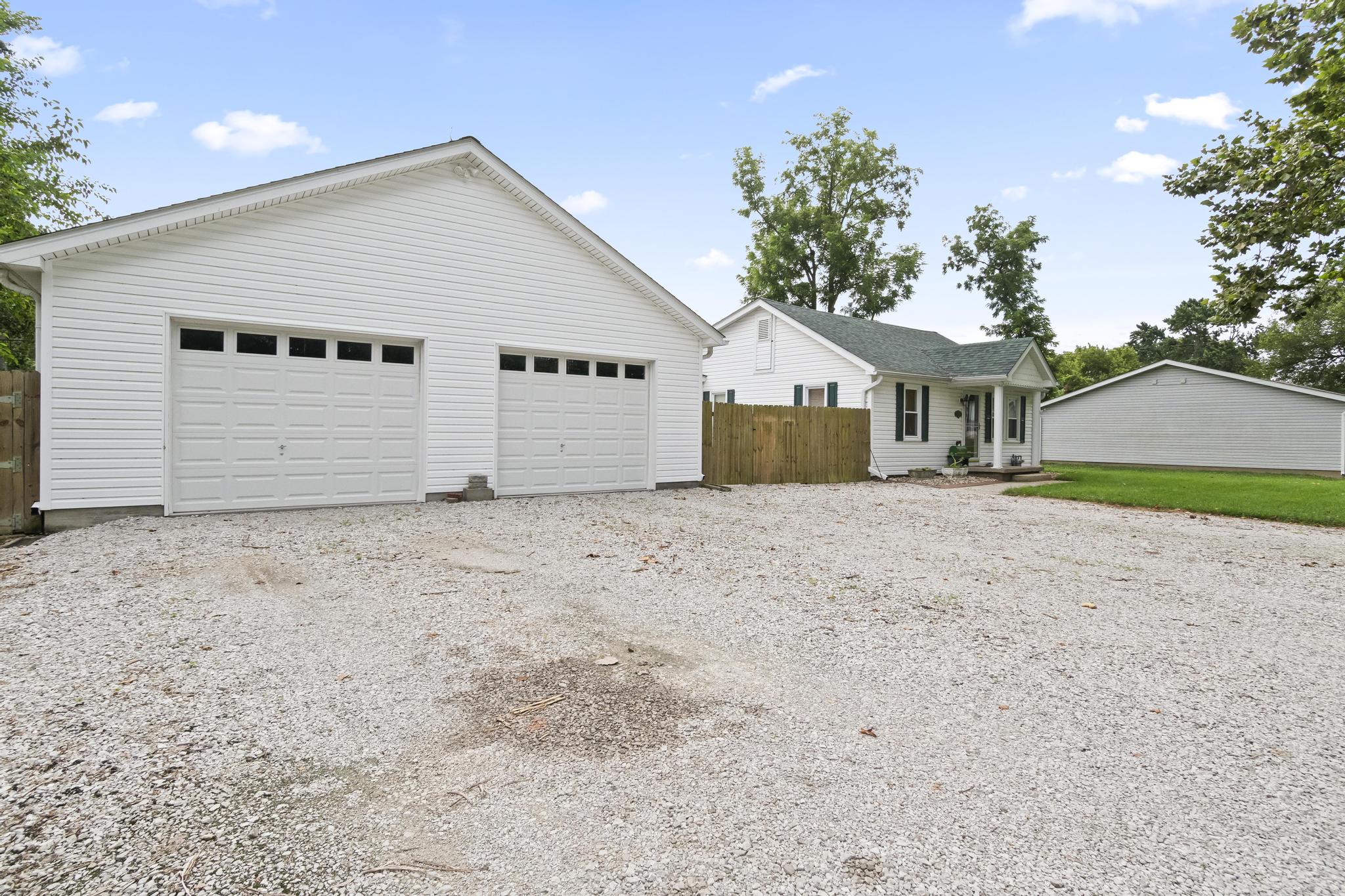 Front view of detached two bay garage and privacy fencing, with gravel driveway and home