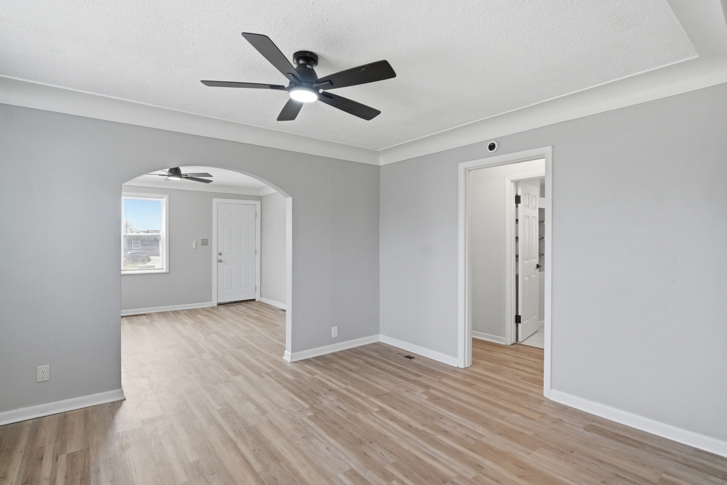 Dining area featuring grey walls, coved ceiling, LVP wood-look flooring, black ceiling fan, featuring an arched doorway looking into the living area with a view of the common hallway at 1929 Beckwith St. Madison.