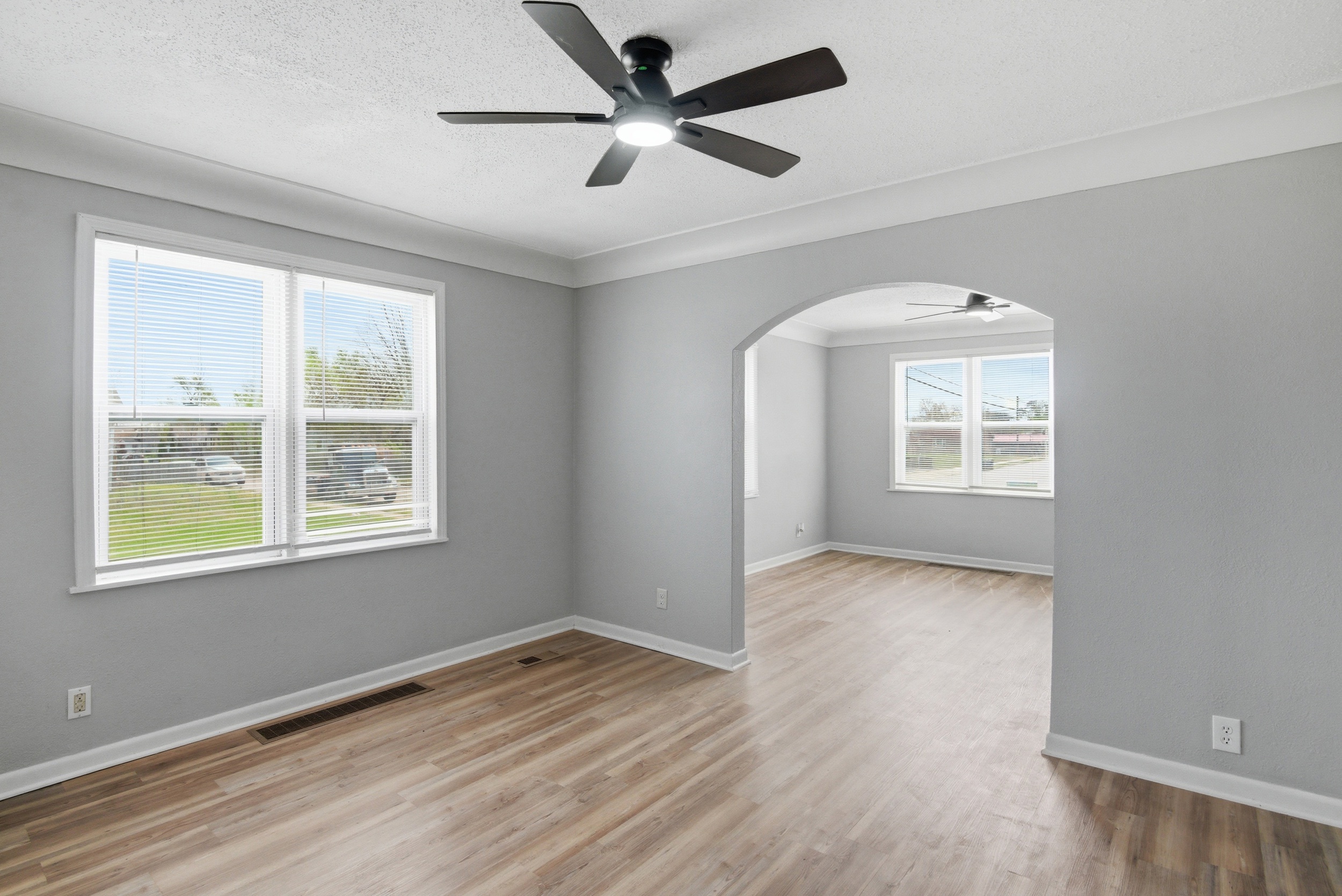 Sun lit dining area with grey walls, coved ceiling, LVP wood-look flooring, double windows, black ceiling fan, featuring an arched doorway looking into the living area at 1929 Beckwith St. Madison.