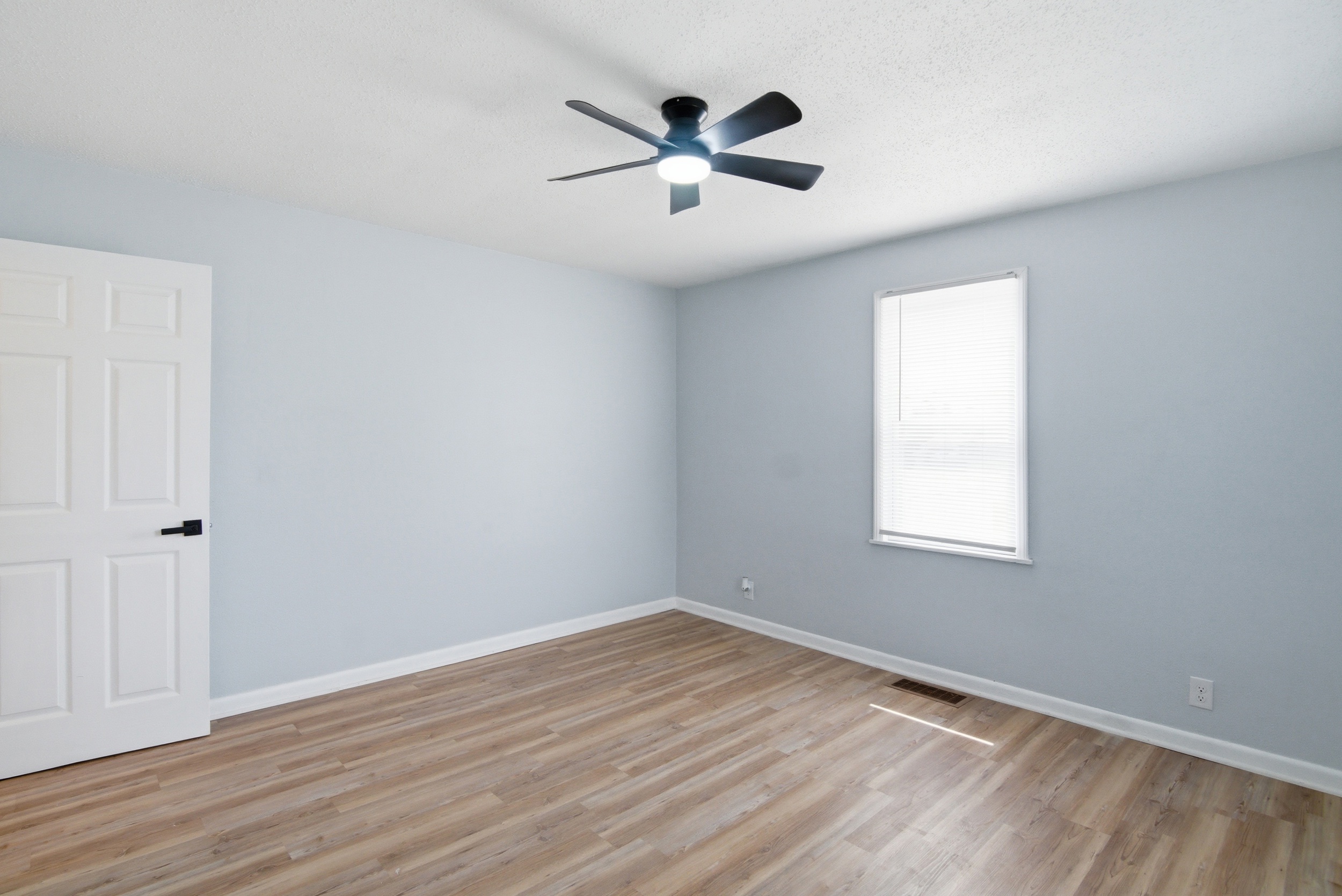 Bright bedroom with grey walls, wood-look flooring, and natural light from a front facing window at 1929 Beckwith St. Madison.