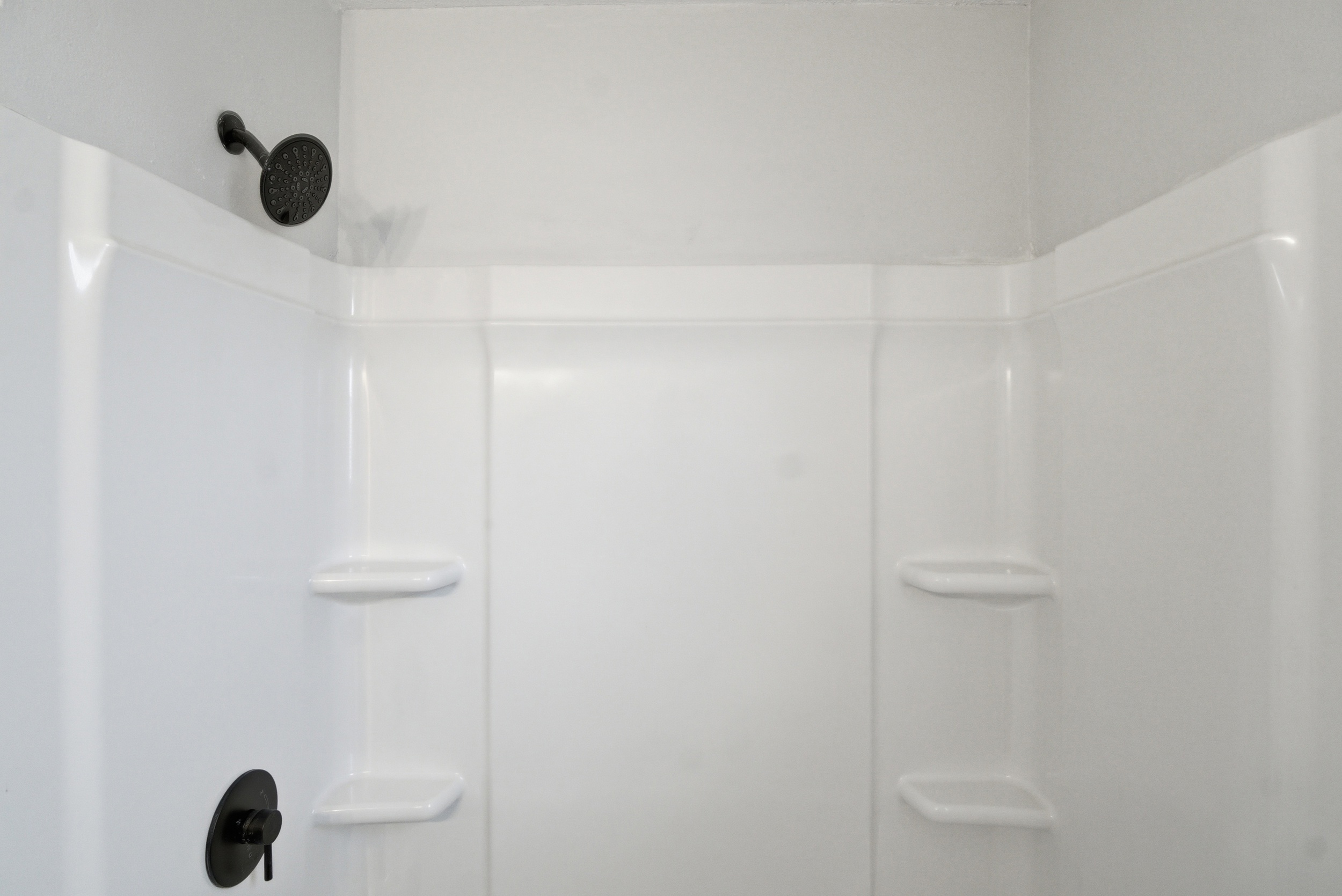 Close-up of bathroom shower surround featuring black shower head and faucet at 1929 Beckwith St. Madison.