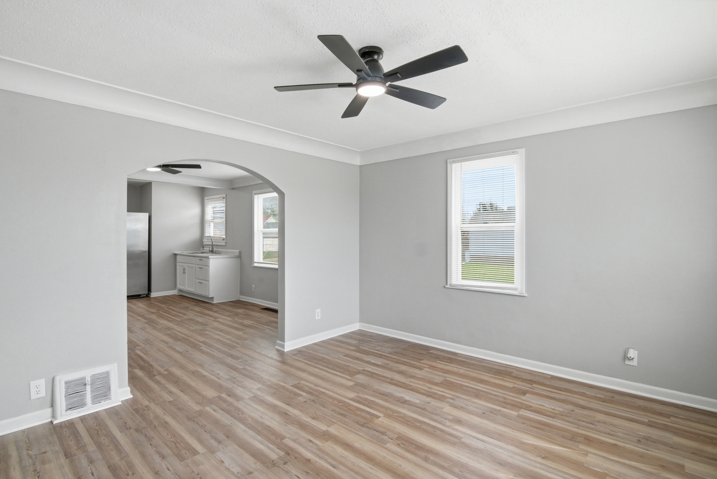Arched doorway and coved ceiling detail in living area with grey walls, and side facing window, featuring LVP wood-look laminate floor, and black ceiling fan at 1929 Beckwith St. Madison.