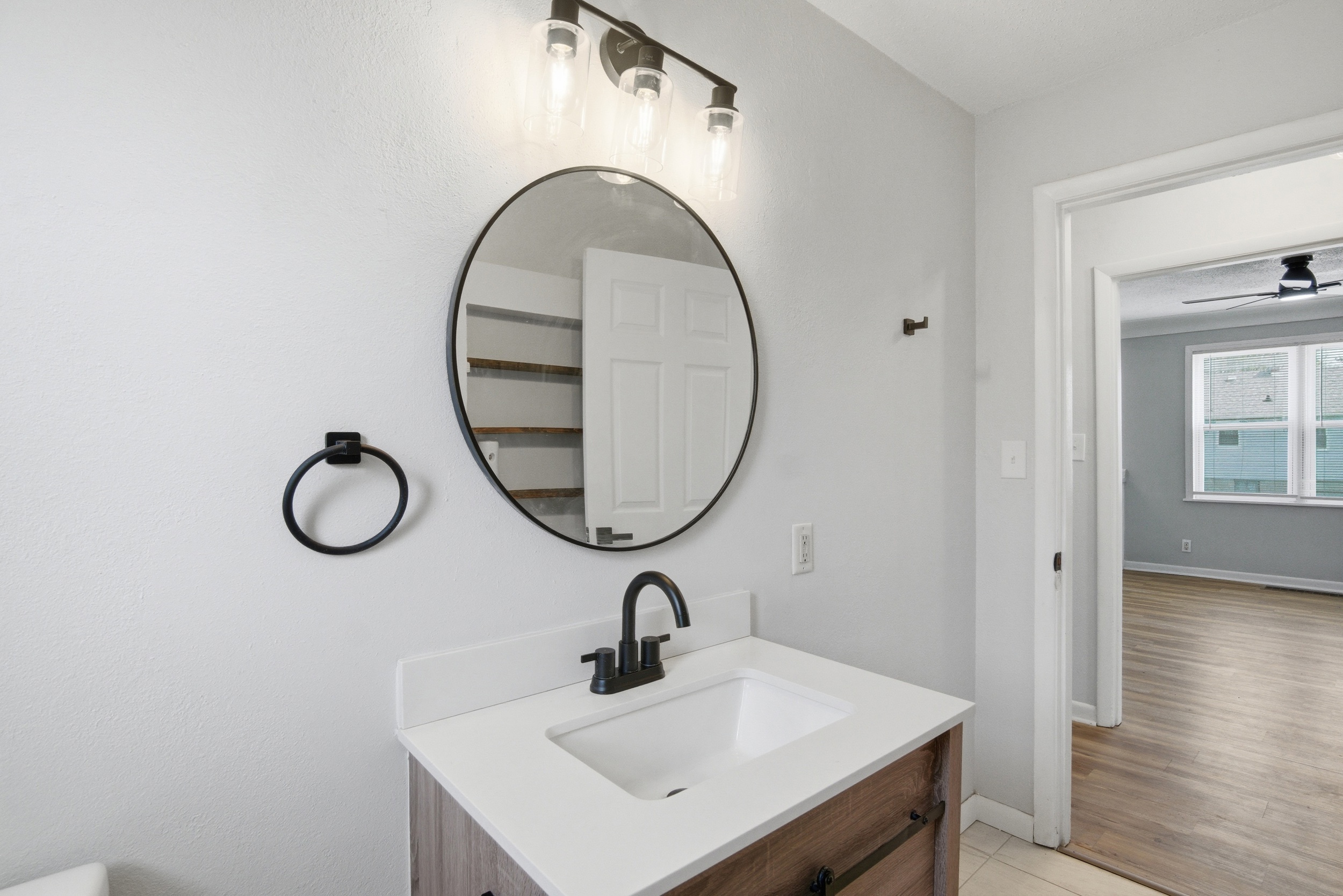 Close-up of the rustic wood-look bathroom vanity, matte black faucet and towel ring, round black-framed mirror, and modern sconce lighting at 1929 Beckwith St. Madison.