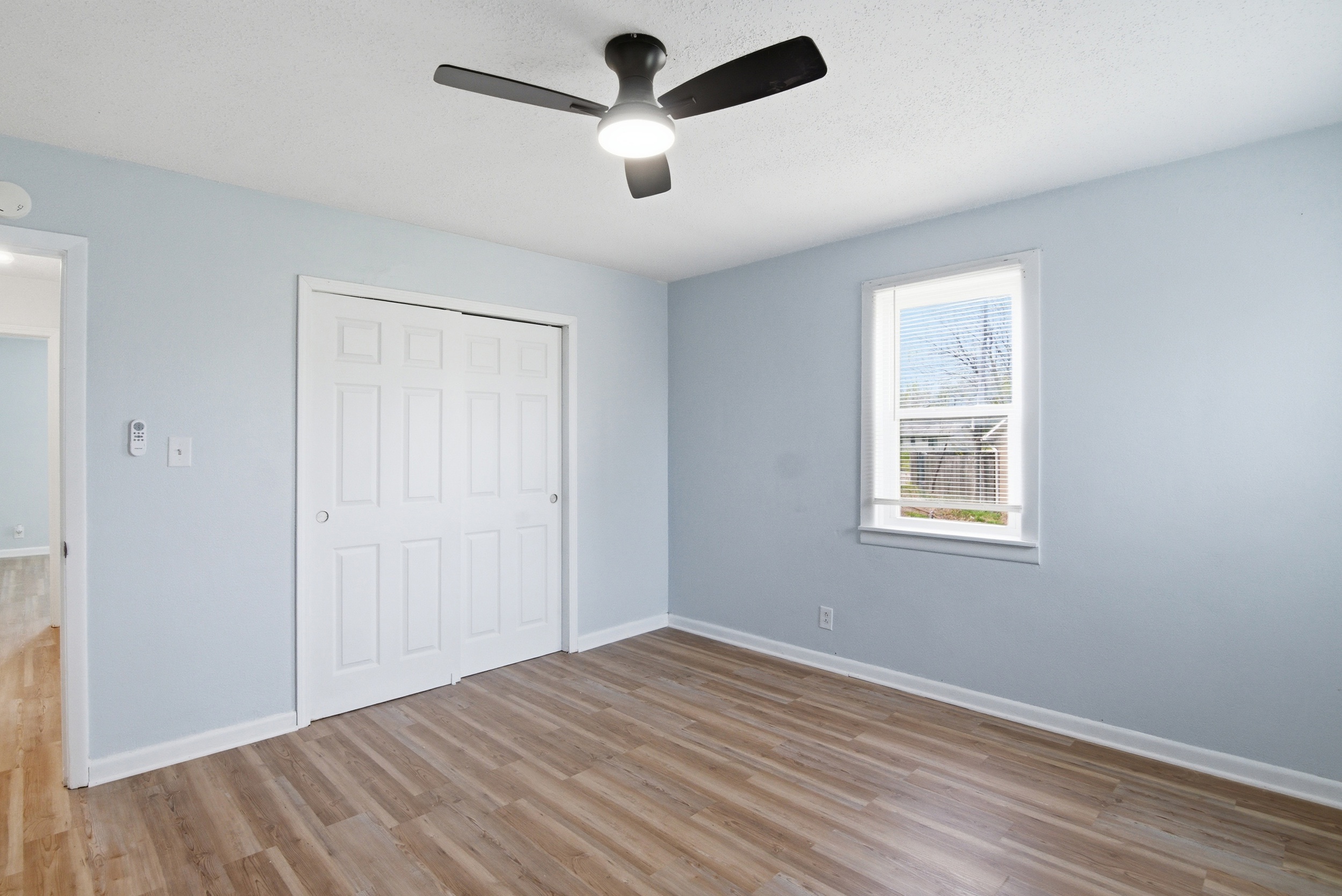 Wood-look LVP flooring, window with blinds, double sliding closet doors and black ceiling fan in primary bedroom at 1929 Beckwith St. Madison.