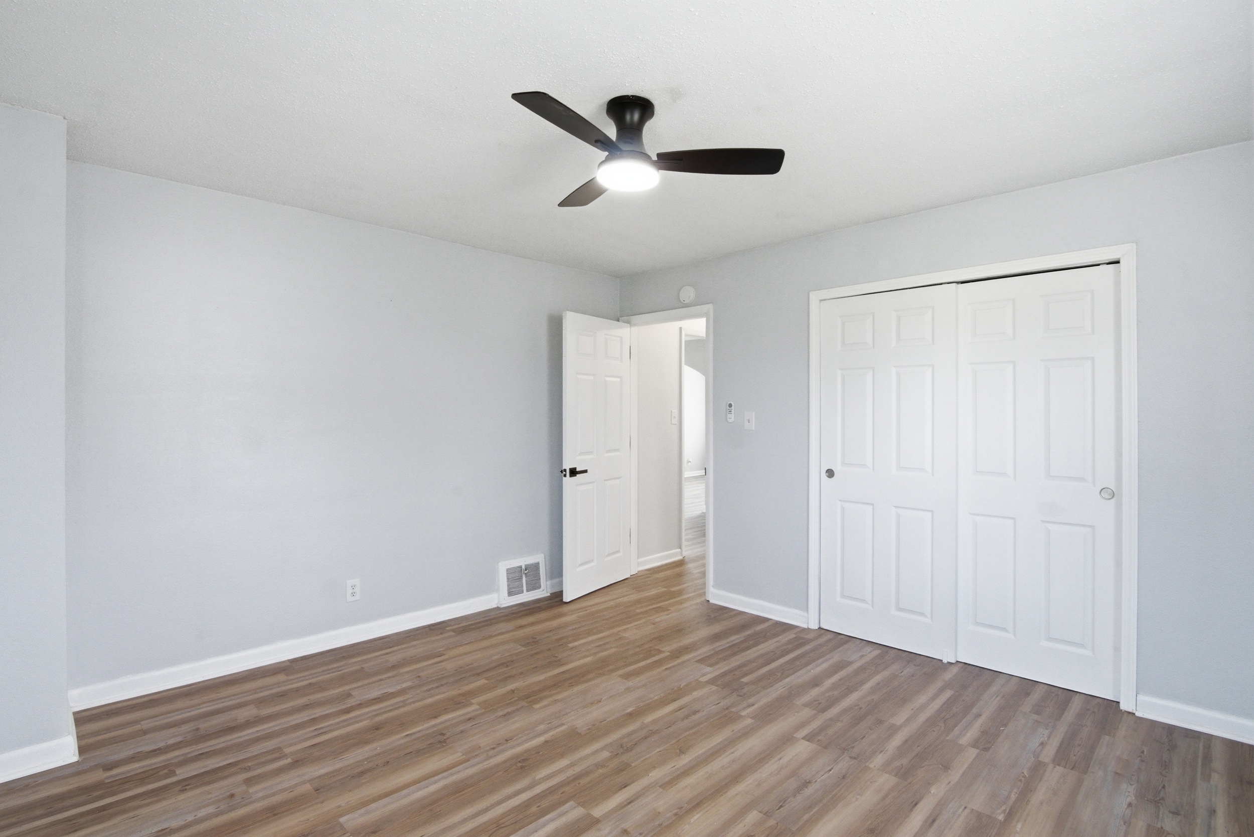 Primary bedroom area with grey walls, wood-looking- laminate flooring, black ceiling fan, and double closet doors at 1929 Beckwith St. Madison.