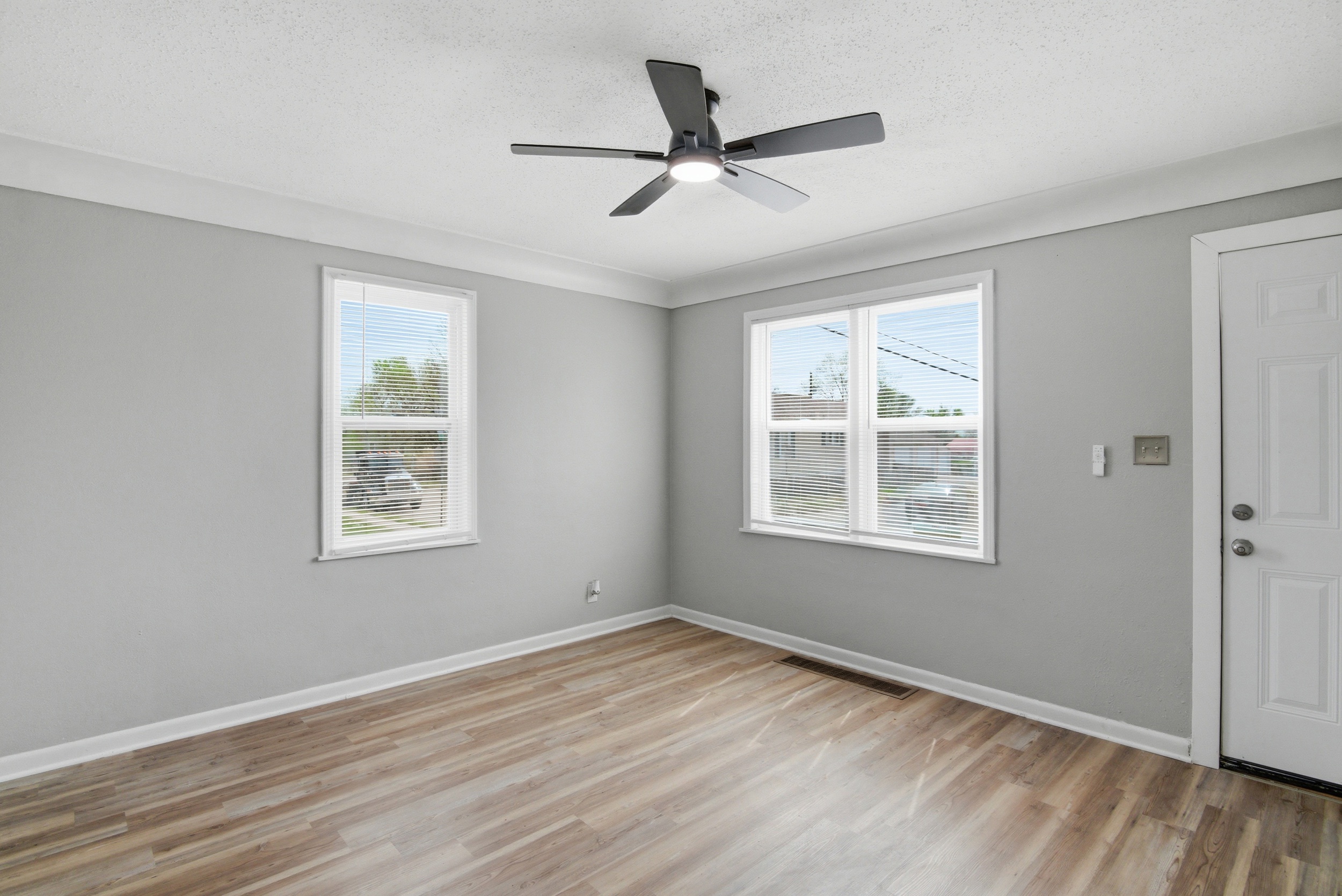 Close-up of Living area with grey walls, front and side facing windows, featuring coved ceiling, LVP wood-look laminate floor, and black ceiling fan at 1929 Beckwith St. Madison.