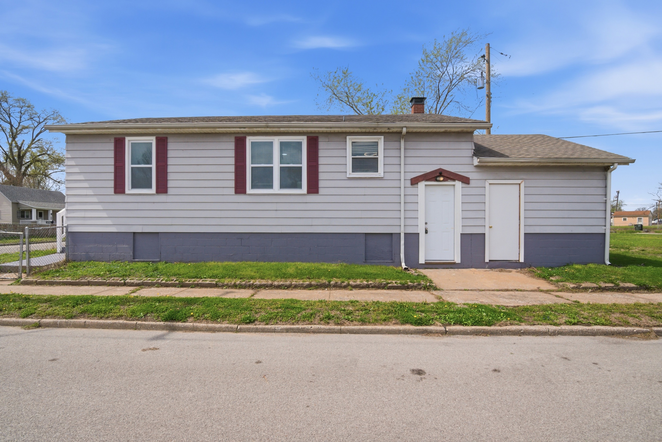 Exterior side of the property featuring grey siding, dark maroon shutters, two white doors, small concrete pad and concrete sidewalk at 1929 Beckwith St. Madison.a