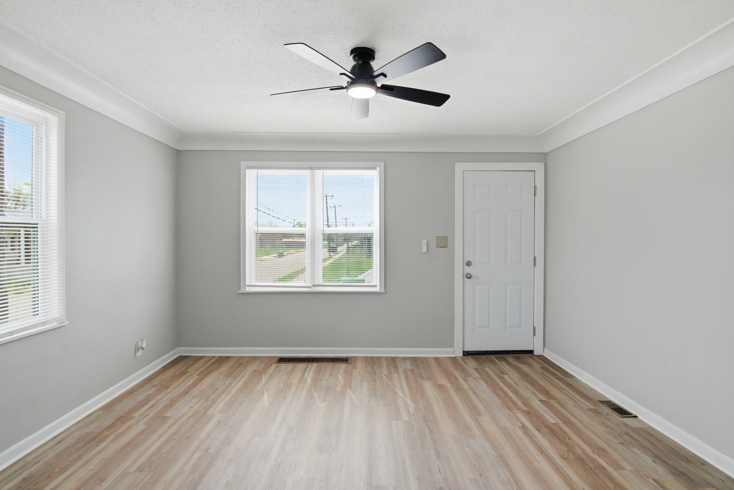 Living area with grey walls, front and side facing windows, featuring coved ceiling, LVP wood-look laminate floor, and black ceiling fan at 1929 Beckwith St. Madison.