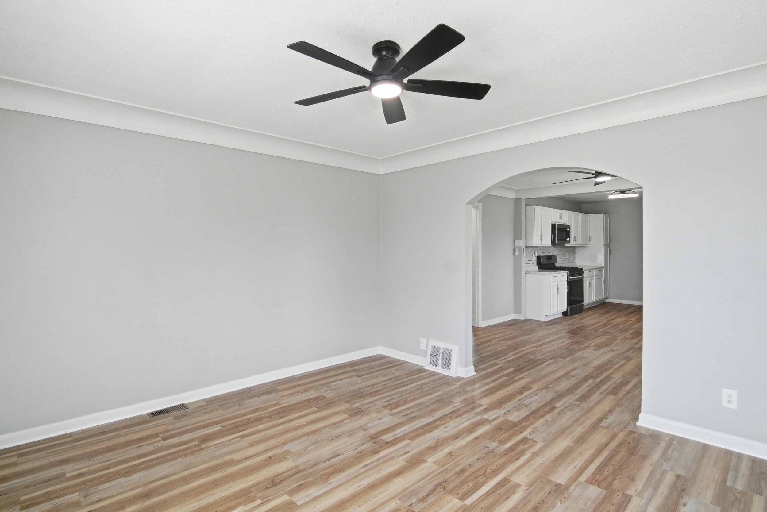 Spacious living area with grey walls, coved ceiling, wood-look laminate flooring, and black ceiling fan, featuring an arched doorway looking into the kitchen at 1929 Beckwith St. Madison.