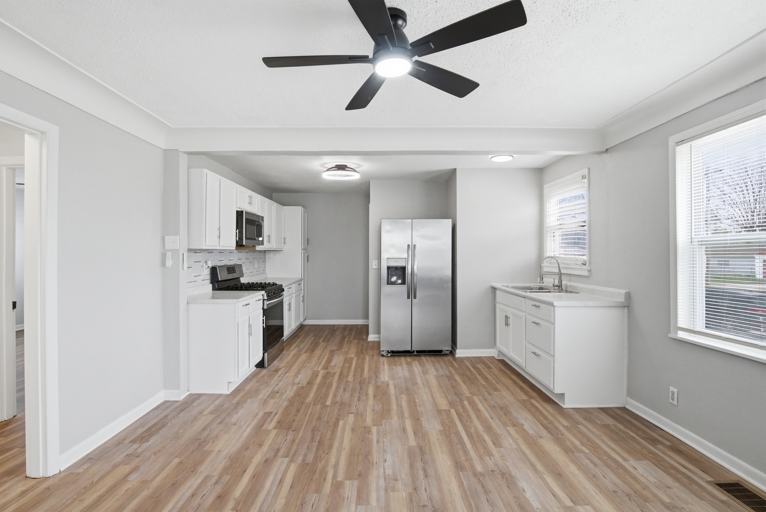 Wide view of modern updated kitchen featuring white shaker cabinets, stainless steel over-the-range microwave and gas stove, grey mosaic tile backsplash, and light countertops at 1929 Beckwith St. Madison.