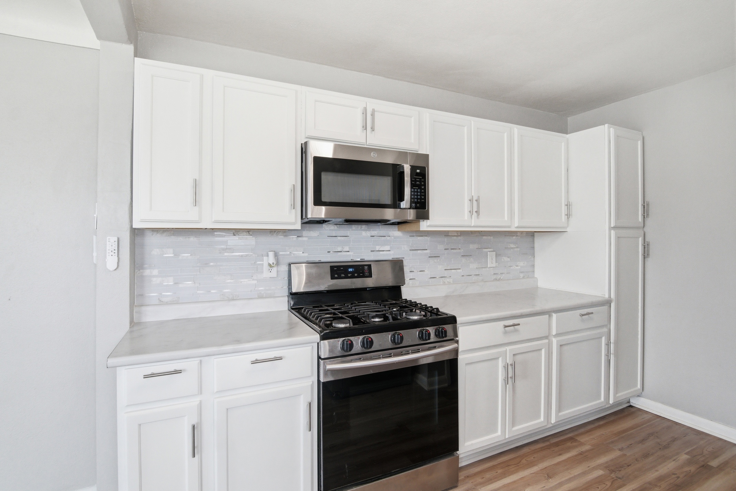 Modern updated kitchen featuring white shaker cabinets, stainless steel over-the-range microwave and gas stove, grey mosaic tile backsplash, and light countertops at 1929 Beckwith St. Madison.