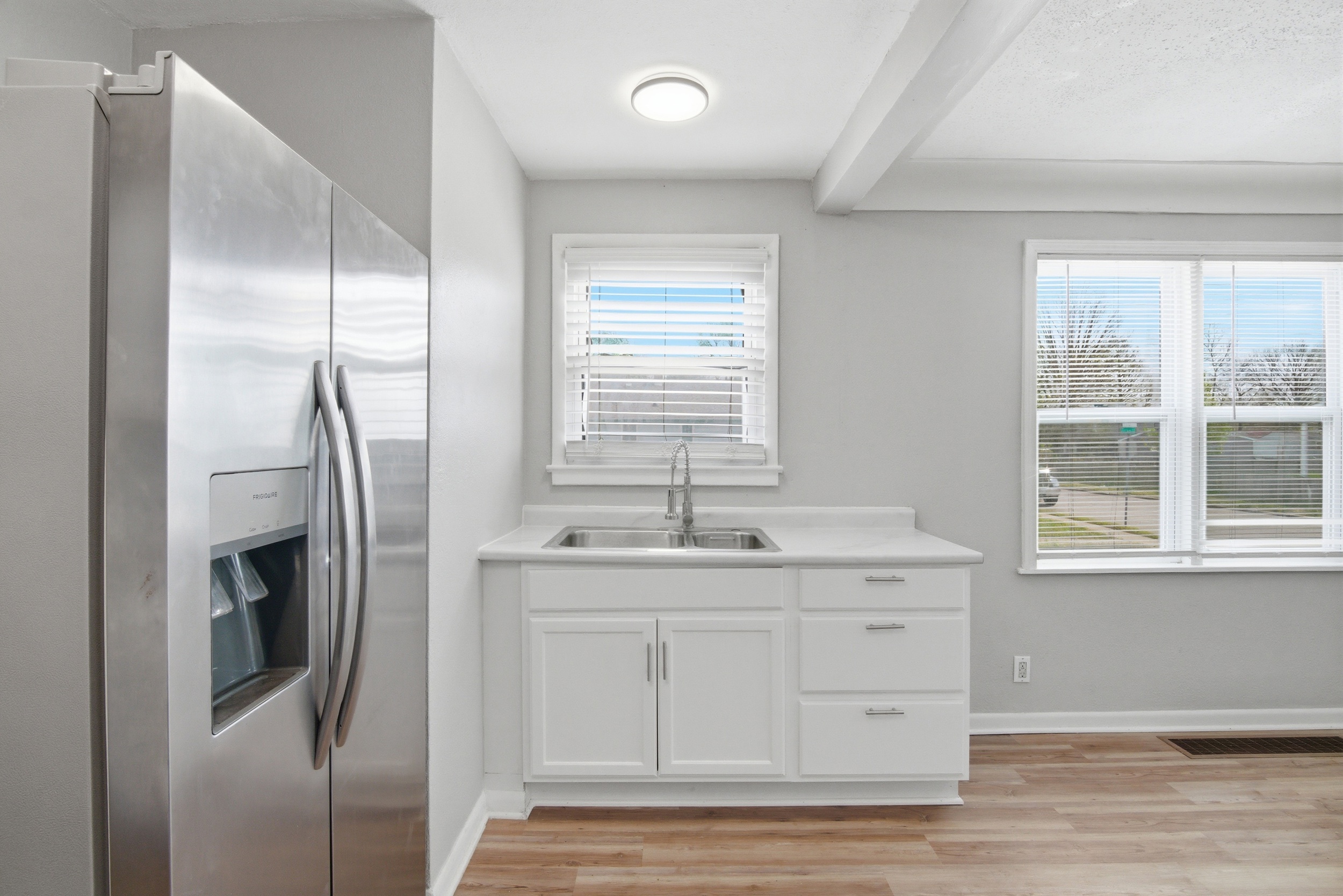 Window with blinds above white kitchen sink cabinetry, stainless steel refrigerator and LVP flooring in kitchen at 1929 Beckwith St. Madison.